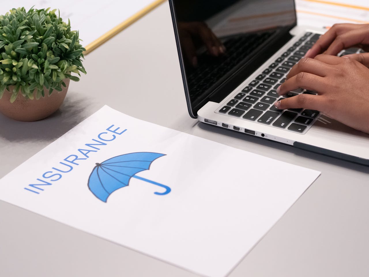 The Art of Drawing Readers In: Your attractive post title goes here Close-up of hands typing on laptop with an insurance document visible on the desk.