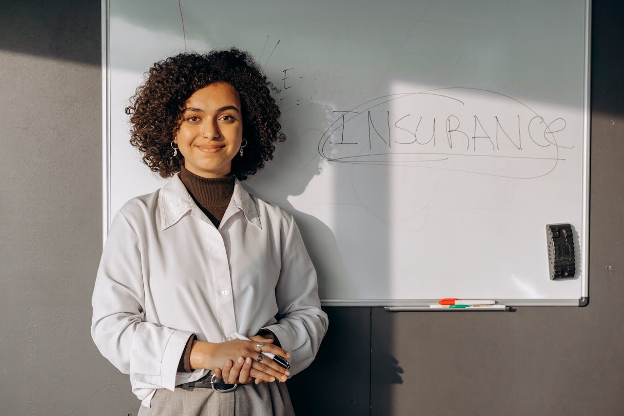 Crafting Captivating Headlines: Your awesome post title goes here Smiling woman with curly hair standing by a whiteboard with insurance written on it, conveying professionalism.